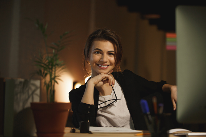 Colaboradora satisfeita com trabalho flexível, sentada à mesa segurando óculos.