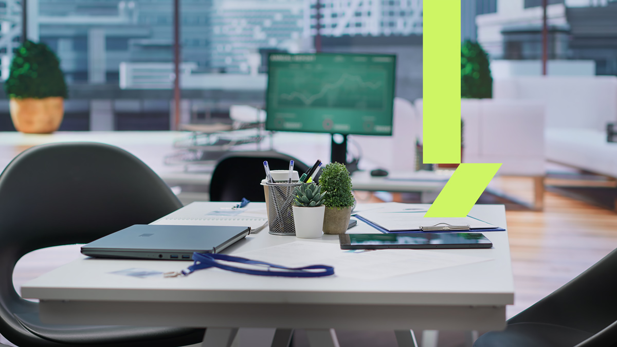 Mesa moderna com notebook fechado, plantas decorativas e materiais de trabalho em ambiente corporativo iluminado, representando aluguel de escritório em espaço flexível.