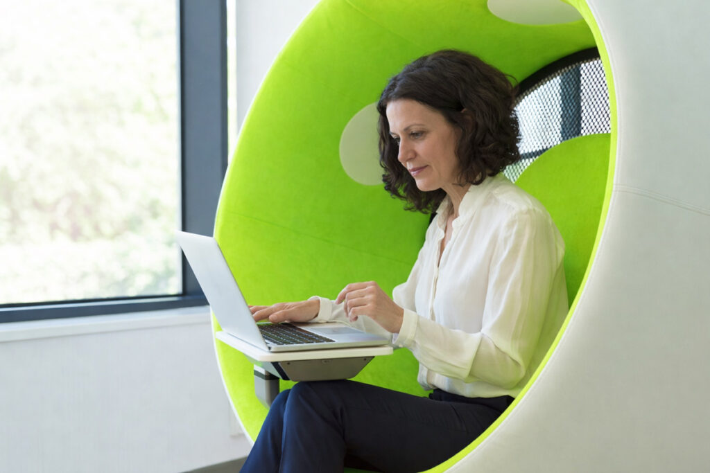 Profissional trabalhando em modelo anywhere office dentro de um trem, usando notebook com vista para o mar, representando trabalho remoto com mobilidade, autonomia e conexão com diferentes lugares.