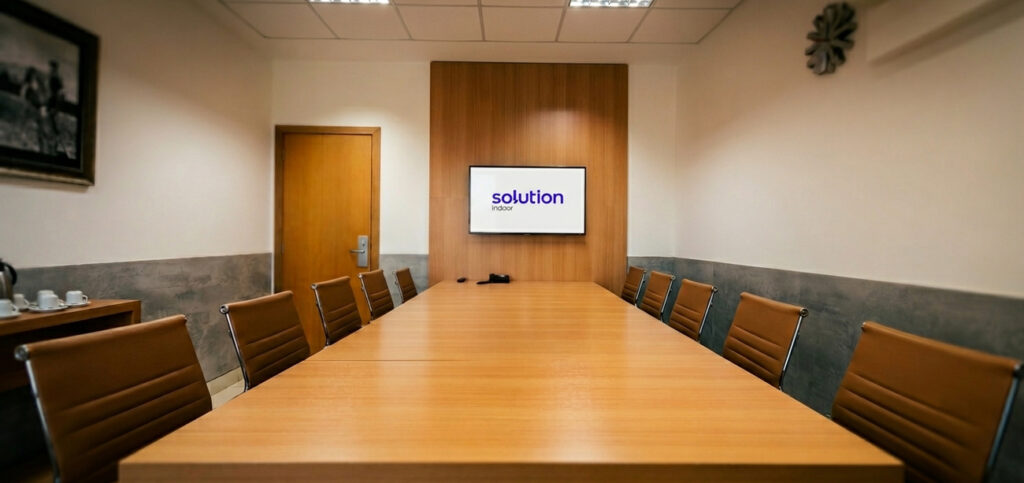 Sala de reunião do smart office Solution Indoor em Ribeirão Preto com mesa longa, com 10 cadeiras e uma televisão ao fundo com o logo da marca.
