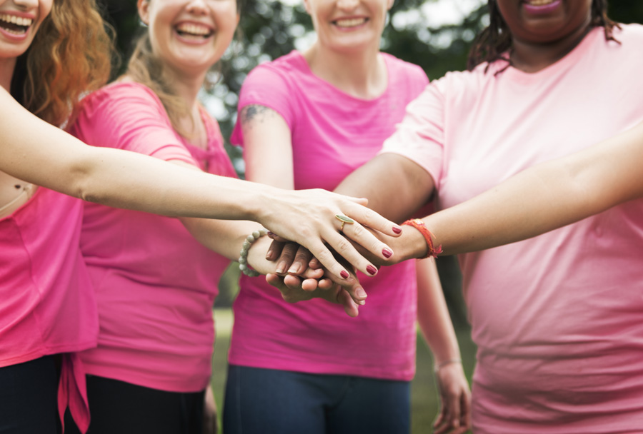 Grupo de mulheres vestindo roupas cor de rosa com as mãos unidas no outubro rosa.